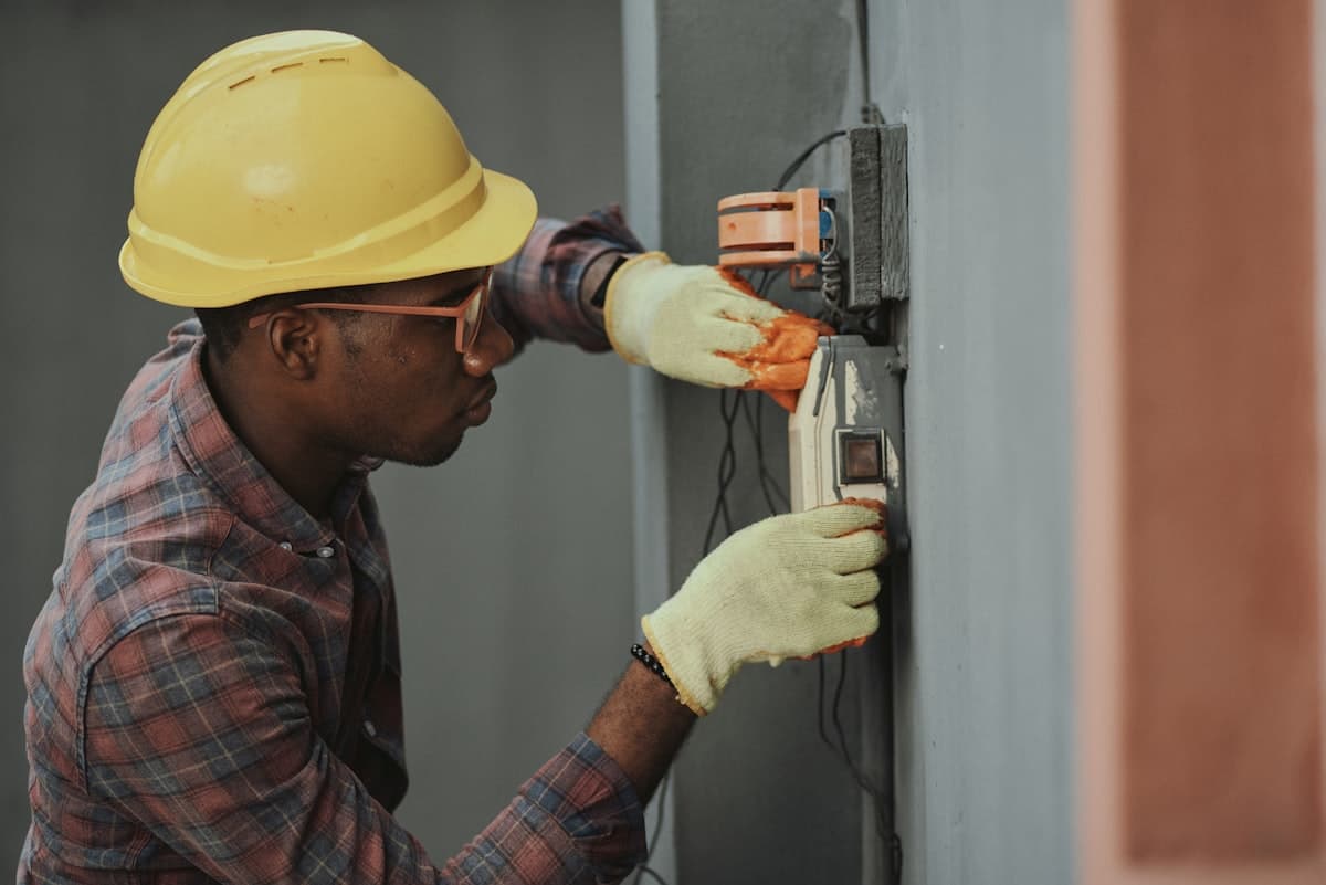 Installateur met helm en handschoenen sluit een wandkast aan